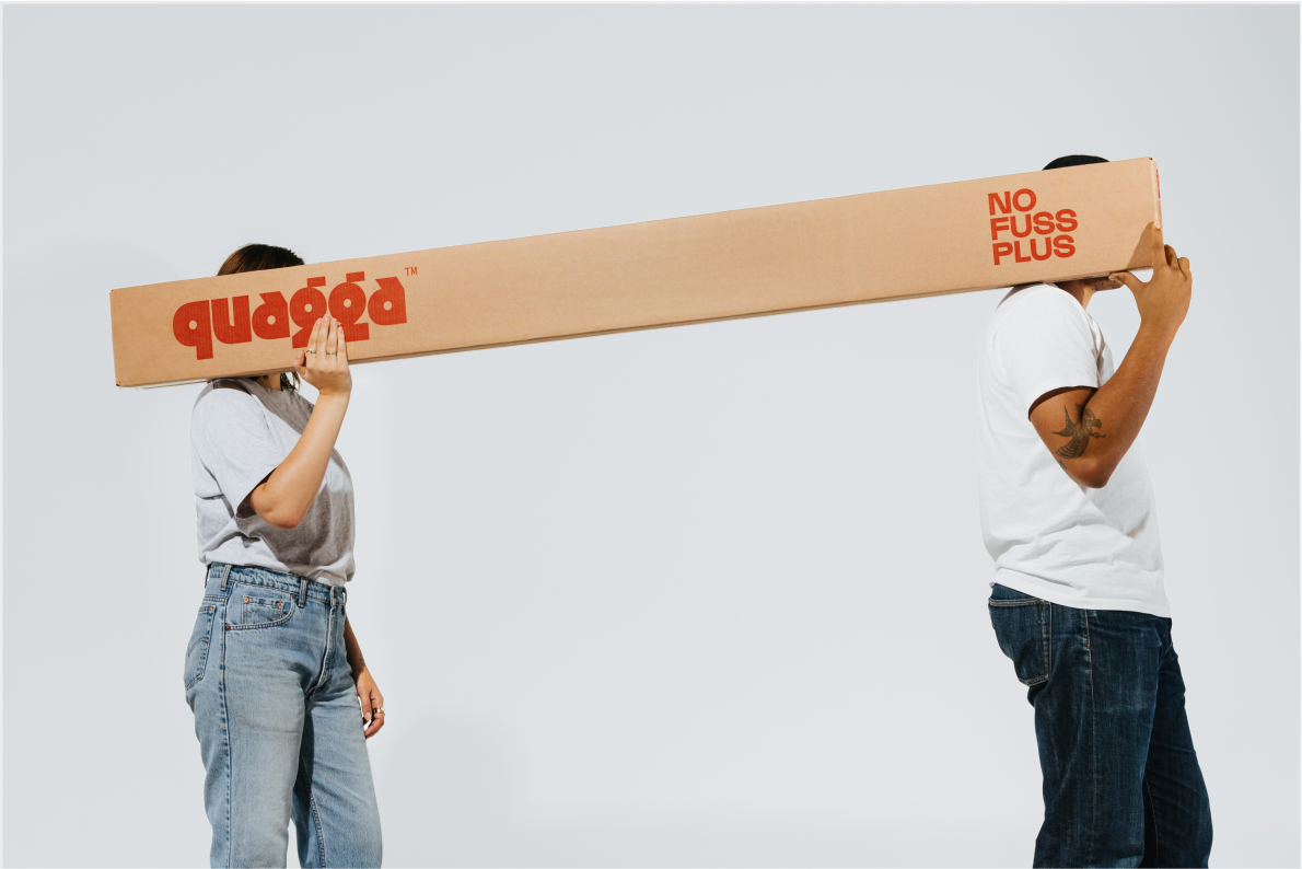 Two people carrying the No Fuss Plus bed frame box by Quagga Designs.