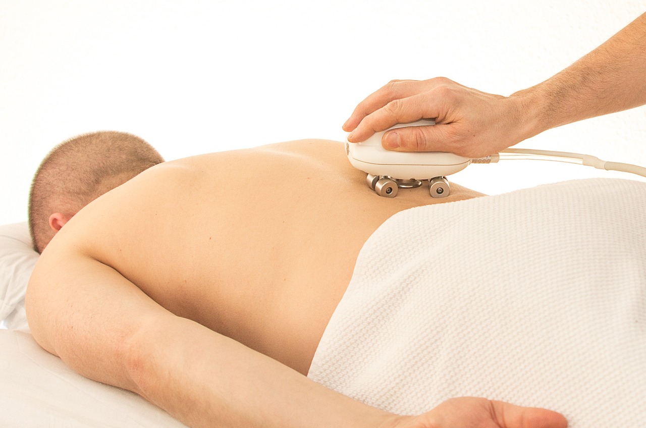 A man lying down on a massage bed with a towel over his body getting a massage with a device 