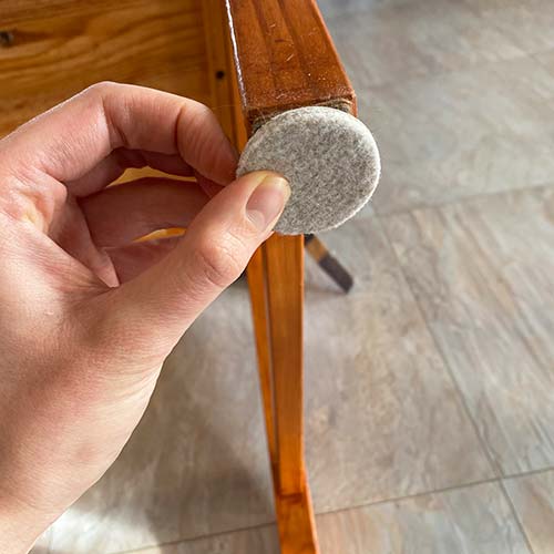 Someone sticking a felt pad onto the leg of a wooden chair