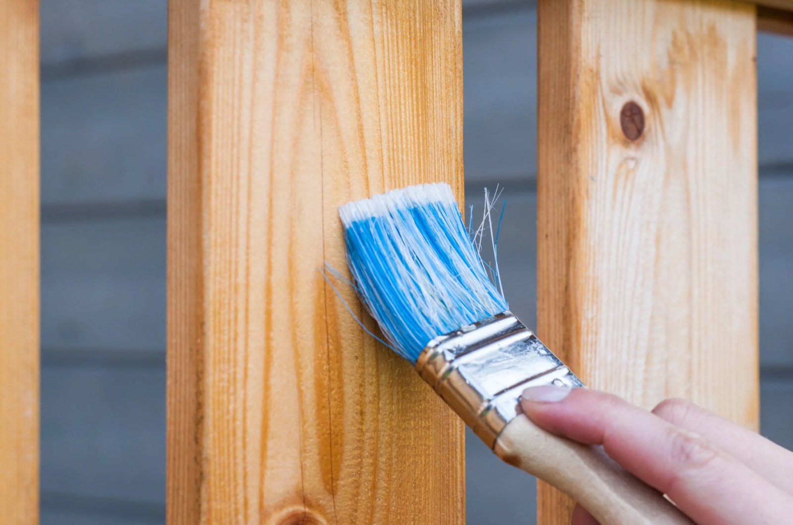 Someone holding a paintbrush and painting varnish on a wood plank.